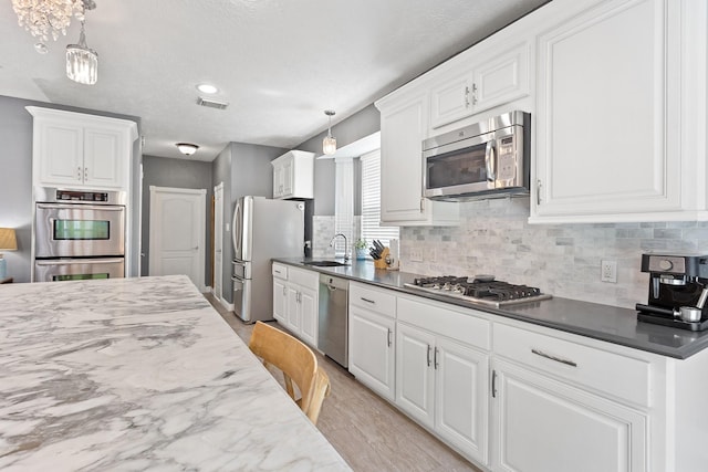kitchen featuring tasteful backsplash, white cabinets, visible vents, stainless steel appliances, and a sink