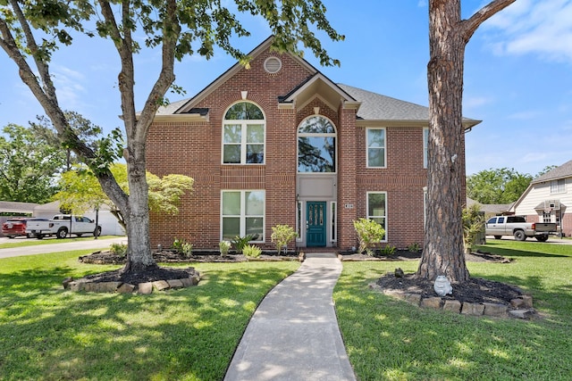 view of front facade featuring a front yard, brick siding, and roof with shingles