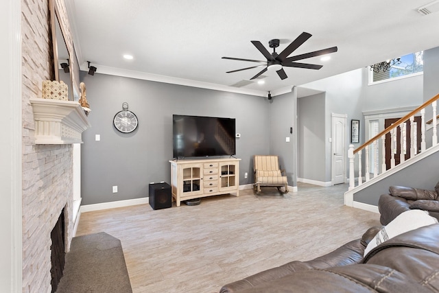living room featuring ceiling fan, a fireplace with raised hearth, visible vents, stairs, and baseboards
