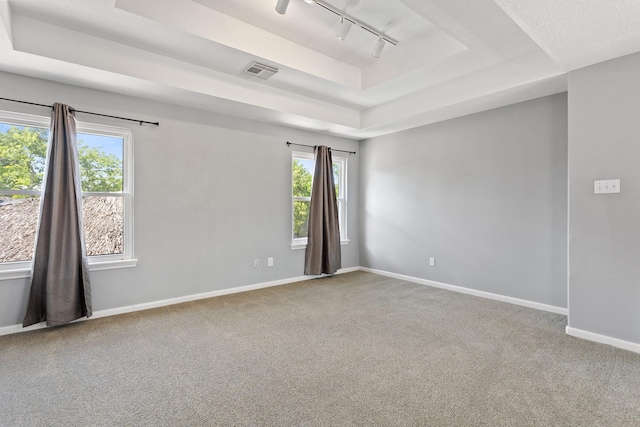empty room featuring a tray ceiling, track lighting, visible vents, and carpet floors