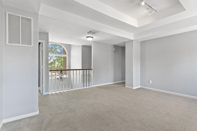 carpeted spare room with rail lighting, a tray ceiling, visible vents, and baseboards