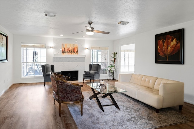 living room featuring a textured ceiling, wood finished floors, a fireplace, baseboards, and visible vents