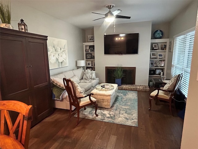 living area with a ceiling fan, dark wood-style floors, built in features, and a fireplace