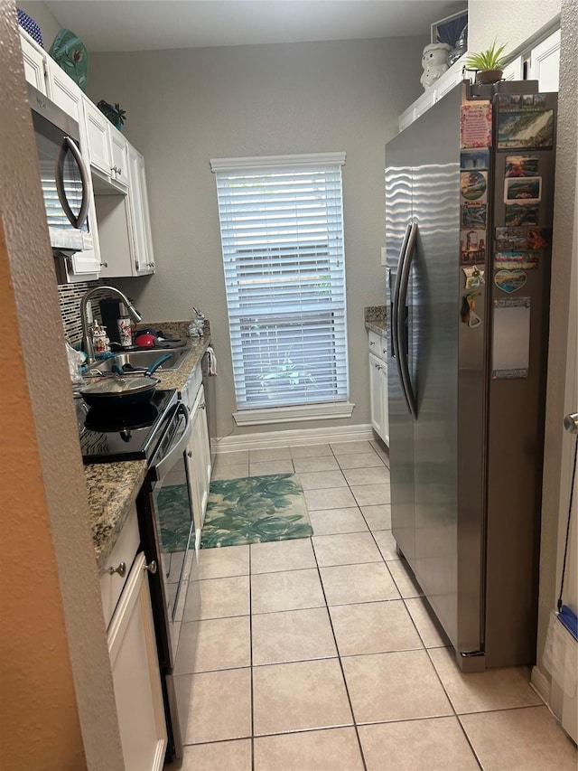 kitchen with appliances with stainless steel finishes, a sink, stone countertops, white cabinetry, and light tile patterned floors