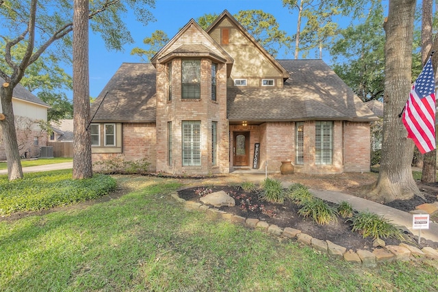 traditional-style home featuring a shingled roof, a front yard, central AC unit, and brick siding