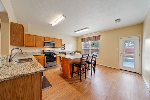 kitchen with a sink, brown cabinetry, a breakfast bar, light wood-type flooring, and stainless steel appliances