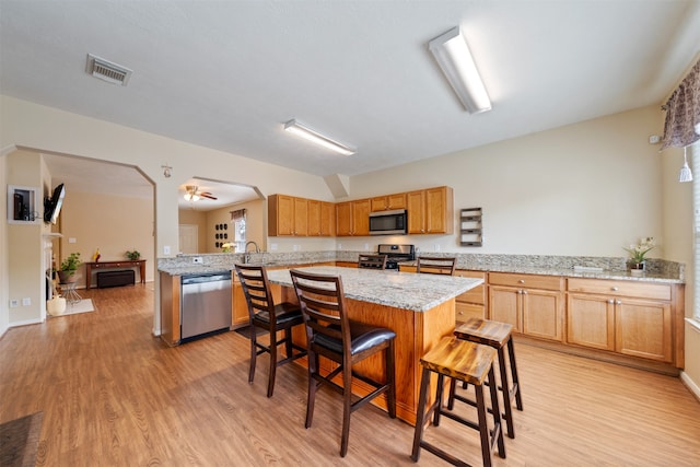 kitchen featuring light wood finished floors, stainless steel appliances, visible vents, a sink, and a breakfast bar area