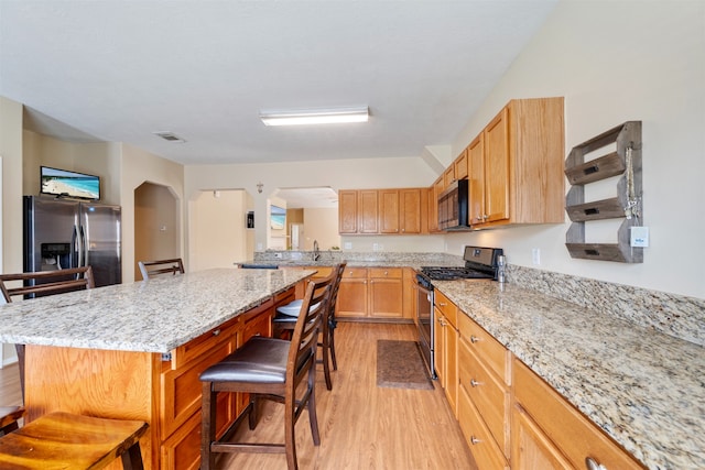kitchen featuring light stone counters, stainless steel appliances, a breakfast bar, arched walkways, and light wood-style flooring