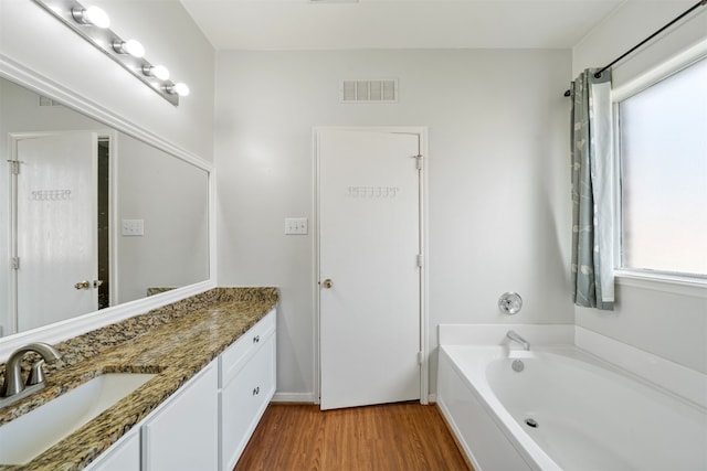 bathroom featuring a garden tub, wood finished floors, visible vents, and vanity