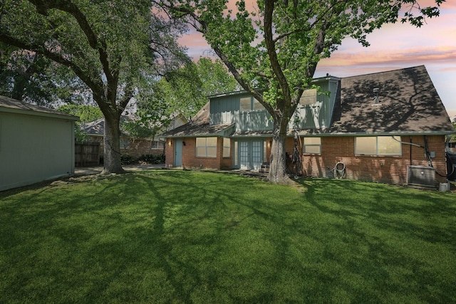 back of property featuring a lawn, fence, and brick siding