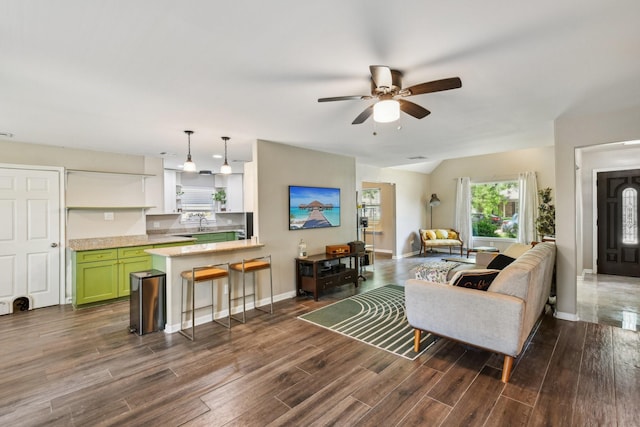 living area with baseboards, ceiling fan, vaulted ceiling, and dark wood-style floors