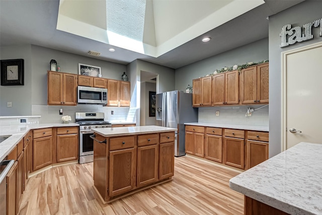 kitchen with light wood finished floors, tasteful backsplash, stainless steel appliances, and light countertops