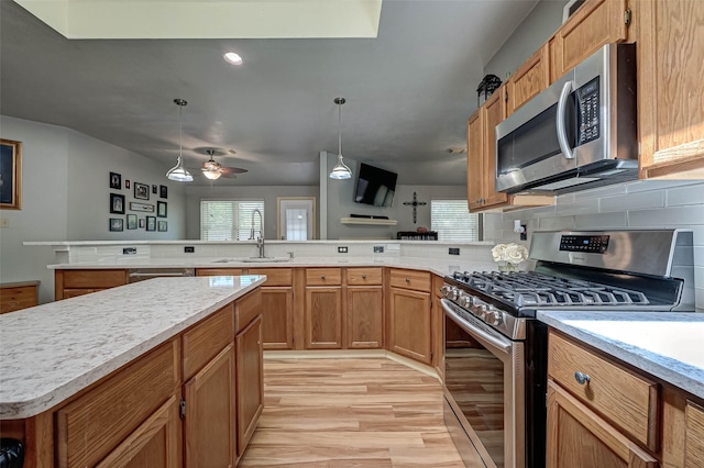 kitchen featuring a sink, light wood-type flooring, a peninsula, light countertops, and appliances with stainless steel finishes