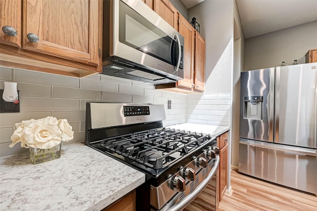 kitchen featuring light wood finished floors, brown cabinets, appliances with stainless steel finishes, and tasteful backsplash