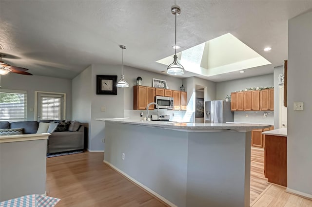 kitchen with stainless steel appliances, light wood-type flooring, a ceiling fan, a peninsula, and light countertops