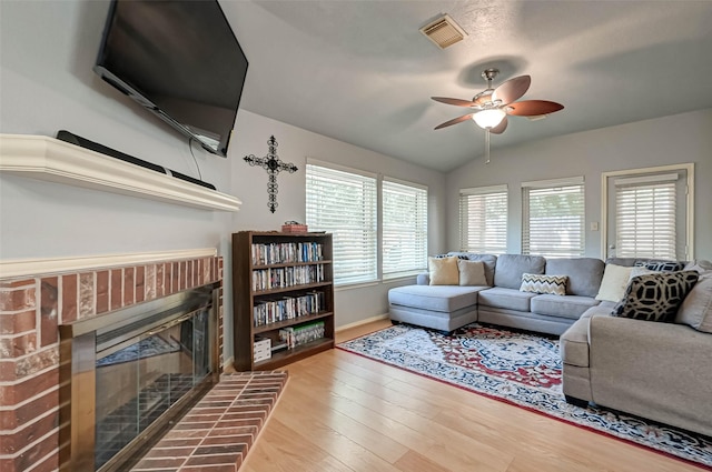 living area featuring wood finished floors, ceiling fan, a brick fireplace, visible vents, and lofted ceiling