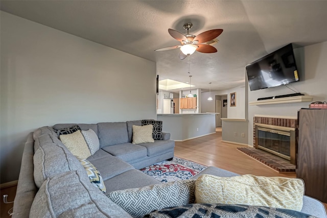 living area with a brick fireplace, a ceiling fan, light wood-style flooring, and baseboards