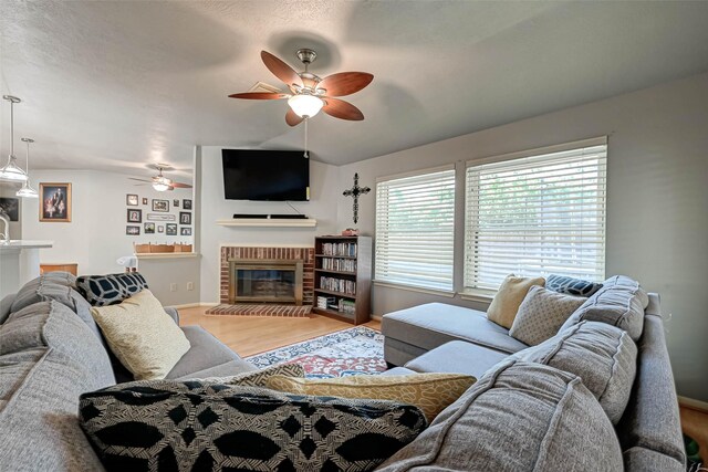 living room featuring a fireplace, wood finished floors, baseboards, and ceiling fan