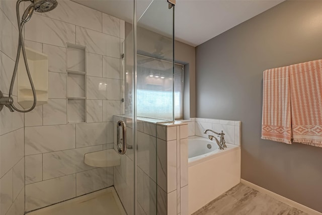 bathroom featuring a garden tub, a shower stall, and baseboards