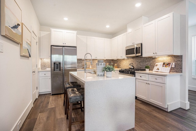 kitchen featuring appliances with stainless steel finishes, a sink, dark wood finished floors, decorative backsplash, and light countertops