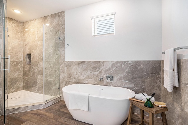 bathroom featuring tile walls, a shower stall, a freestanding bath, wood finished floors, and wainscoting