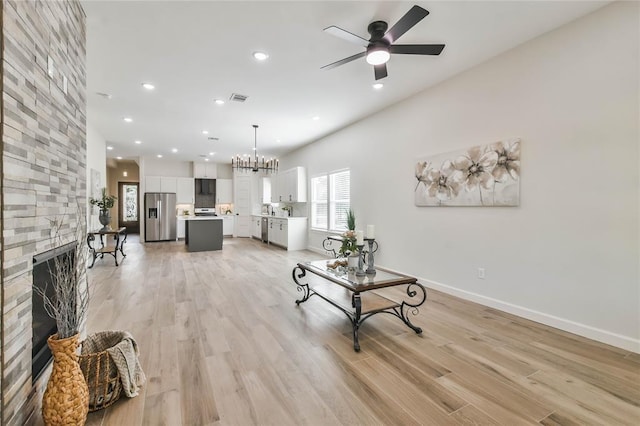 620 Lily St, Waller, TX 77484 - living area featuring a stone fireplace, recessed lighting, light wood-style flooring, visible vents, and ceiling fan with notable chandelier