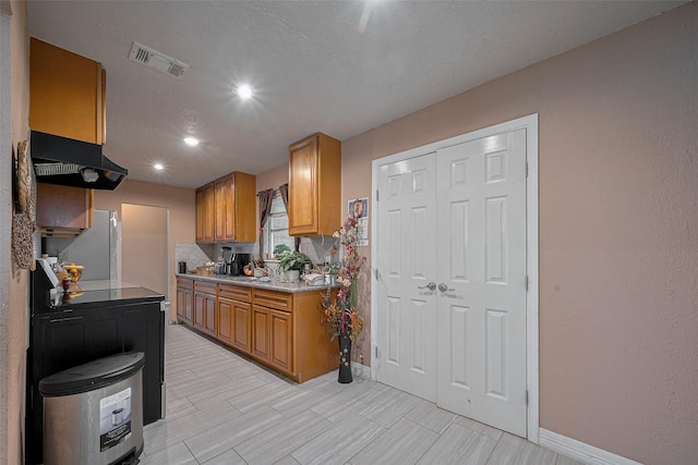 9034 Talton St, Houston, TX 77078 - kitchen with visible vents, baseboards, freestanding refrigerator, under cabinet range hood, and brown cabinets