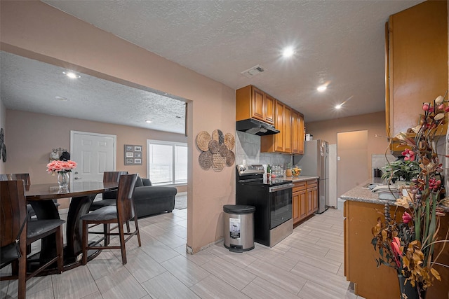 9034 Talton St, Houston, TX 77078 - kitchen with recessed lighting, a textured ceiling, under cabinet range hood, brown cabinetry, and appliances with stainless steel finishes