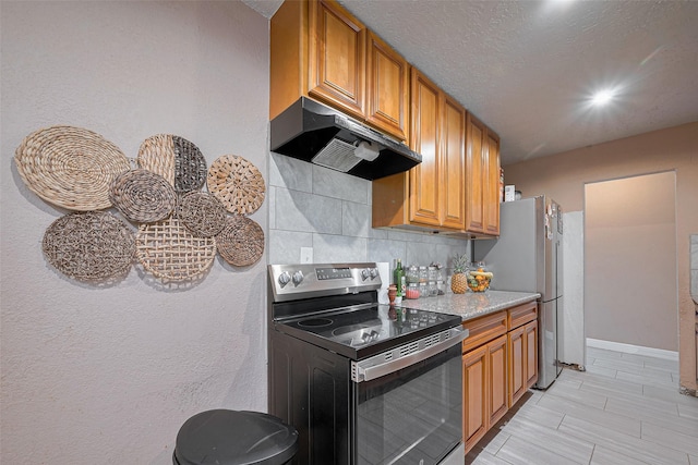 9034 Talton St, Houston, TX 77078 - kitchen with light countertops, under cabinet range hood, brown cabinets, decorative backsplash, and appliances with stainless steel finishes