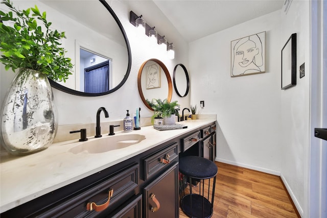 bathroom with wood finished floors, double vanity, a sink, and baseboards