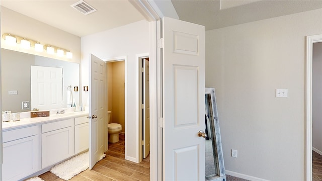 bathroom featuring visible vents, toilet, a sink, wood tiled floor, and double vanity