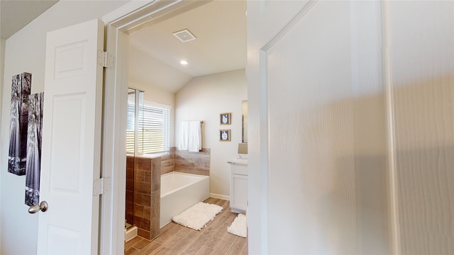 full bathroom with a bath, vanity, vaulted ceiling, visible vents, and wood finished floors