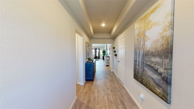 corridor featuring light wood-style flooring, baseboards, recessed lighting, and a raised ceiling