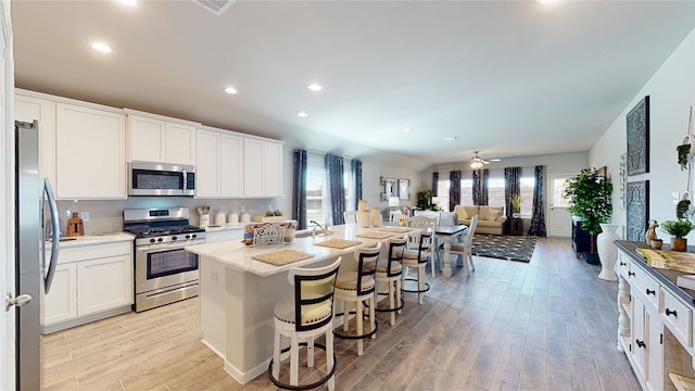 kitchen with light wood-style floors, white cabinetry, appliances with stainless steel finishes, a kitchen island with sink, and a breakfast bar area