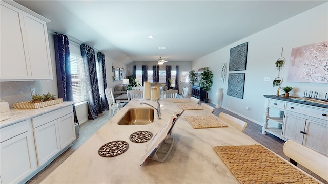 kitchen featuring open floor plan, white cabinetry, a ceiling fan, backsplash, and a sink