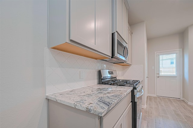 17726 Pamukkale Pl, Tomball, TX 77377 - kitchen featuring stainless steel appliances, decorative backsplash, baseboards, light wood-type flooring, and light stone countertops