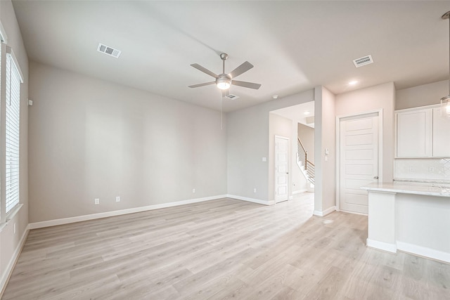 unfurnished living room with visible vents, a ceiling fan, stairway, and light wood finished floors