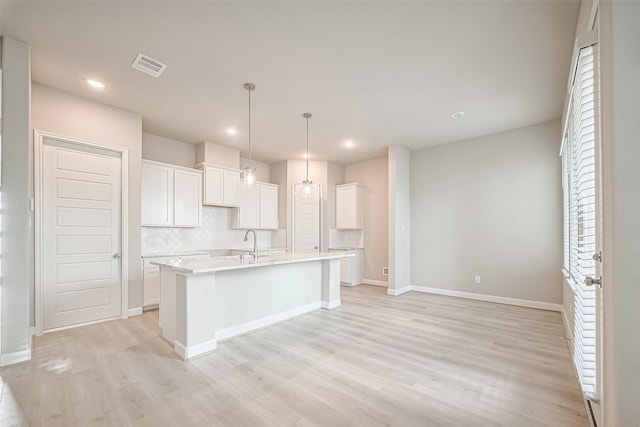 kitchen featuring an island with sink, light wood-style flooring, backsplash, white cabinets, and visible vents