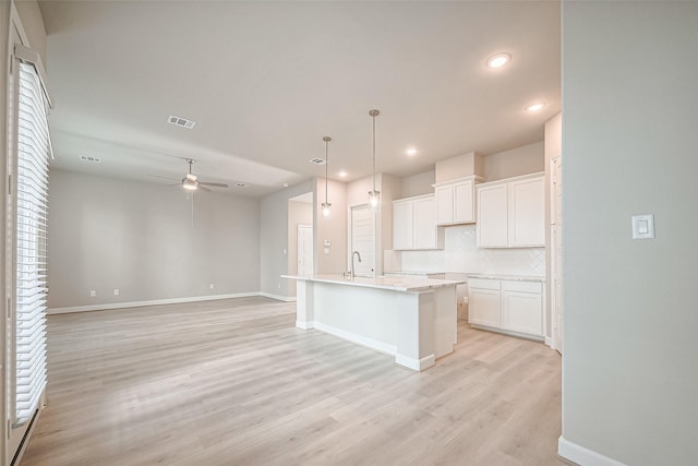 kitchen featuring light wood-style flooring, tasteful backsplash, white cabinetry, a ceiling fan, and a sink