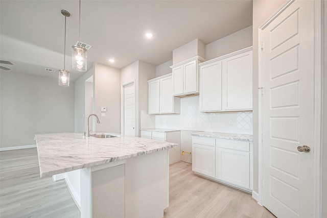 kitchen featuring tasteful backsplash, white cabinets, light stone countertops, light wood finished floors, and a sink