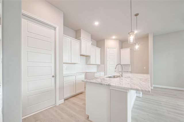 kitchen featuring light wood-type flooring, light stone counters, white cabinetry, a sink, and hanging light fixtures