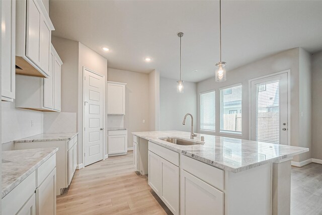 kitchen with a sink, light wood-style floors, recessed lighting, a center island with sink, and light stone countertops