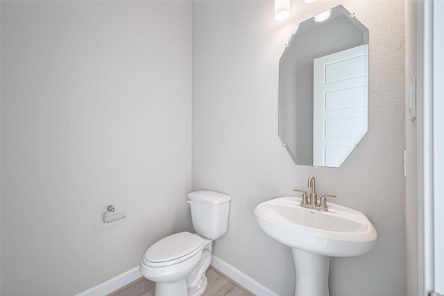 half bathroom with toilet, baseboards, wood finished floors, and a sink