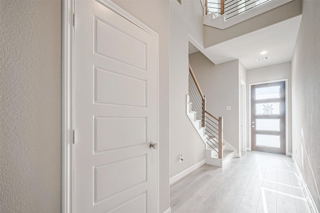 foyer with visible vents, baseboards, a textured wall, stairway, and light wood finished floors