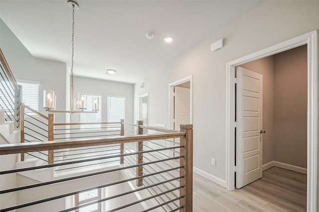 hall with plenty of natural light, light wood finished floors, baseboards, and an inviting chandelier