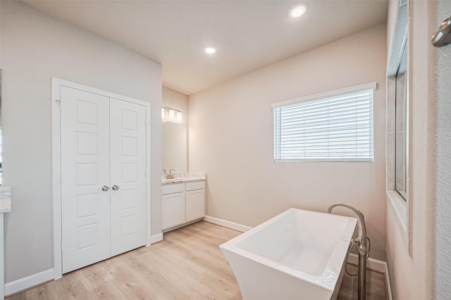 full bathroom featuring vanity, baseboards, recessed lighting, a freestanding bath, and wood finished floors