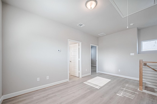 empty room featuring visible vents, light wood-style flooring, attic access, and baseboards