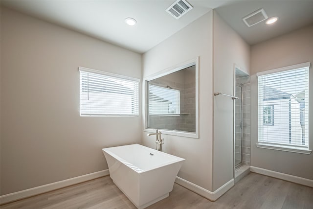 bathroom with visible vents, baseboards, a freestanding bath, a tile shower, and wood finished floors