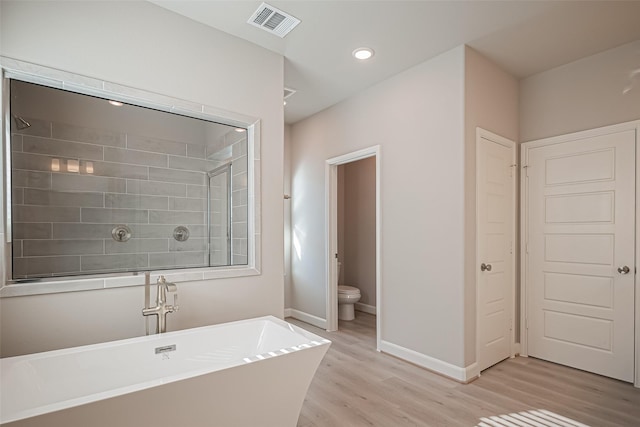 full bathroom with baseboards, toilet, visible vents, a freestanding bath, and wood finished floors