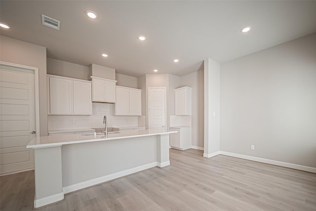 kitchen featuring white cabinetry, a center island with sink, decorative backsplash, light wood finished floors, and a sink